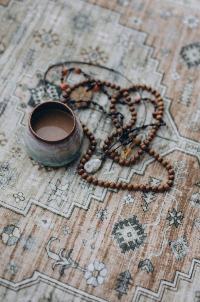 Zeremonieller Kakao in einer Keramiktasse auf Teppich mit indigenem Muster, daneben Mala, Ayahuasca-Liane und Steinkette