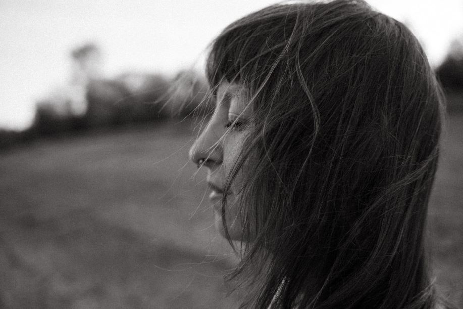 Schwarz-weiß-Porträt von Angelina Katharina Petersen, mit geschlossenen Augen friedlich zur Seite blickend, im Wind vor weiter Landschaft