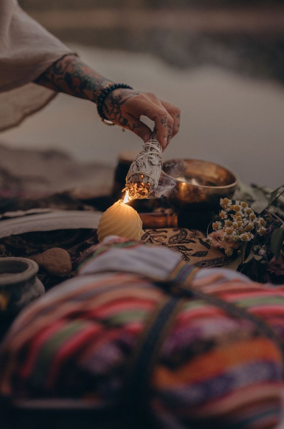 Schamanisches Ritual in Leipzig: Klangschale, Federn, Blumen und ein Mesa, während Angelina Katharina Petersen mit tätowierter Hand Salbei an einer Kerze entzündet