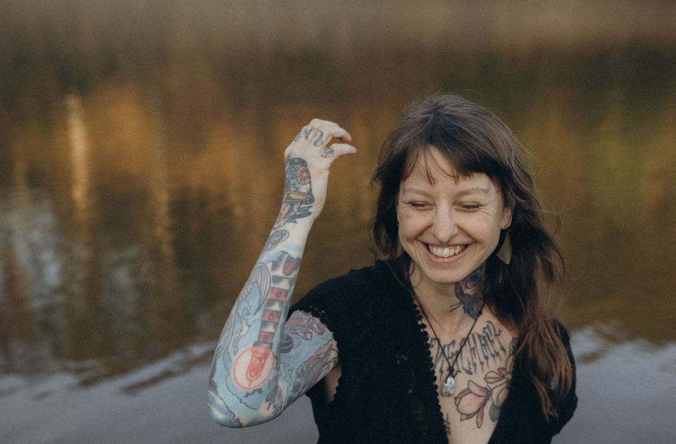 Angelina Katharina Petersen lächelt mit geschlossenen Augen, im Hintergrund Wasser und Natur – ein Moment voller Freude und Leichtigkeit