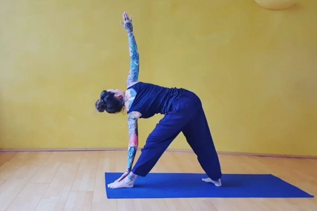 Angelina Katharina Petersen praktiziert Yoga im Raum in Leipzig, Trikonasana auf Yogamatte vor gelbem Hintergrund und Holzboden