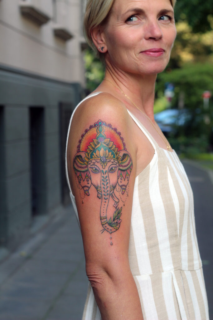 eine Frau von der Seite fotografiert, mit einem Ganesha Tattoo auf dem Oberarm, gestochen von der Tätowiererin von Angelina Katharina Petersen in Leipzig