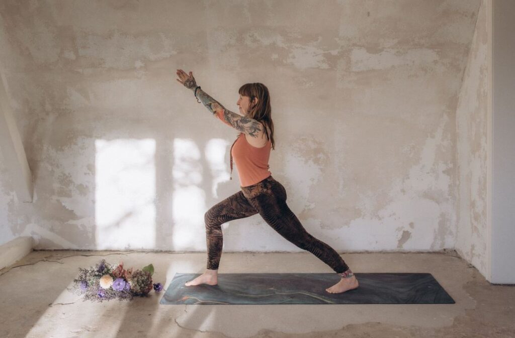Angelina Katharina Petersen, macht das Yoga Asana, Krieger eins, in einem weißen hellen Raum. Sie unterrichtet Yoga in Leipzig