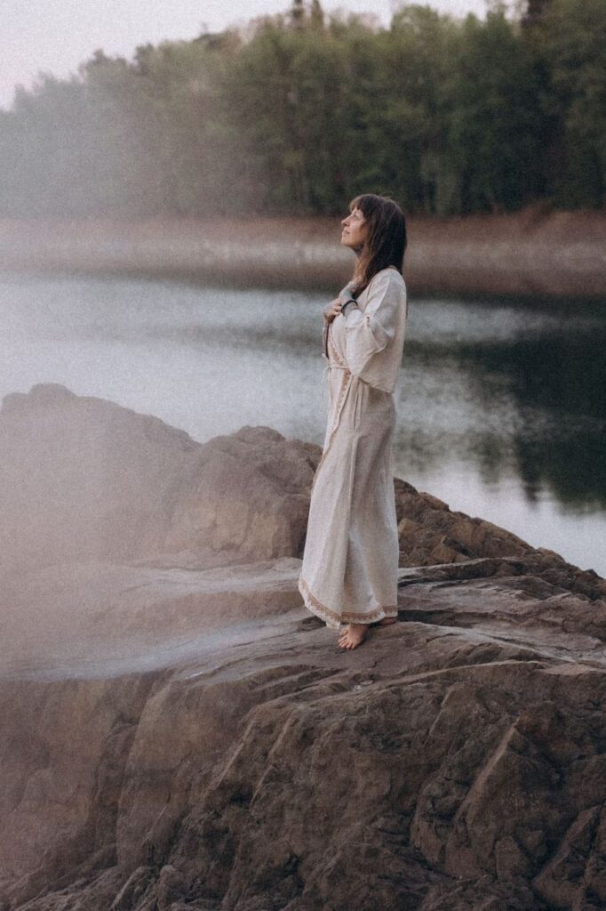Angelina Katharina steht auf einem Felsen am Wasser und schaut nach Oben. Sie begleitet Menschen in schamanischer Tradition in Leipzig und Deutschlandweit